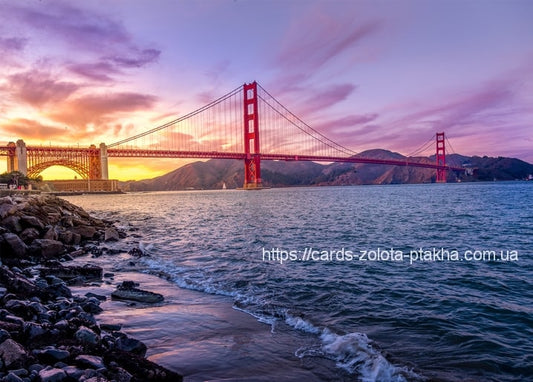 Golden Gate Bridge leuchtet rot bei Sonnenuntergang über einer felsigen Pazifikküste.