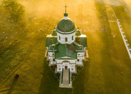 Вигляд з висоти на білу церкву з зеленими банями біля Мостища в золотому вечірньому світлі серед цвинтаря