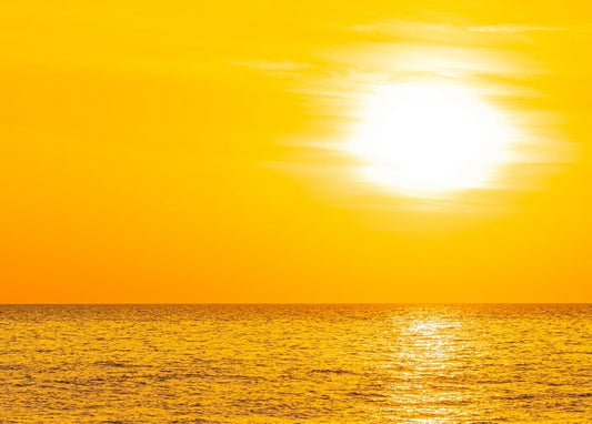 Goldene Sonne geht über ruhigem Meer unter, warmer Lichtschein auf dem Wasser