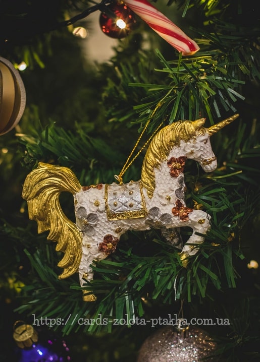 Goldenes Einhorn-Ornament mit Blumenmuster an einem Tannenzweig mit Lichterkette