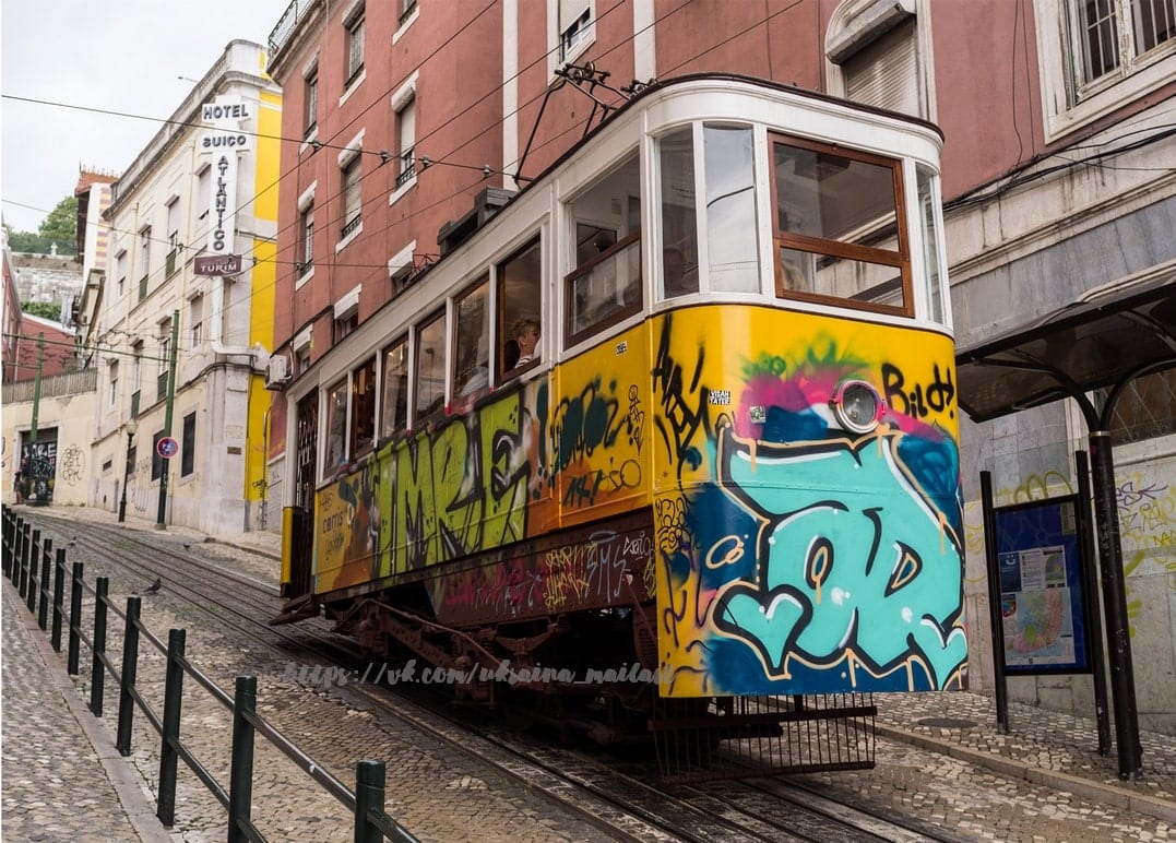 Gelbe Tram voller Graffiti auf einer Kopfsteinpflastergasse in Lissabon