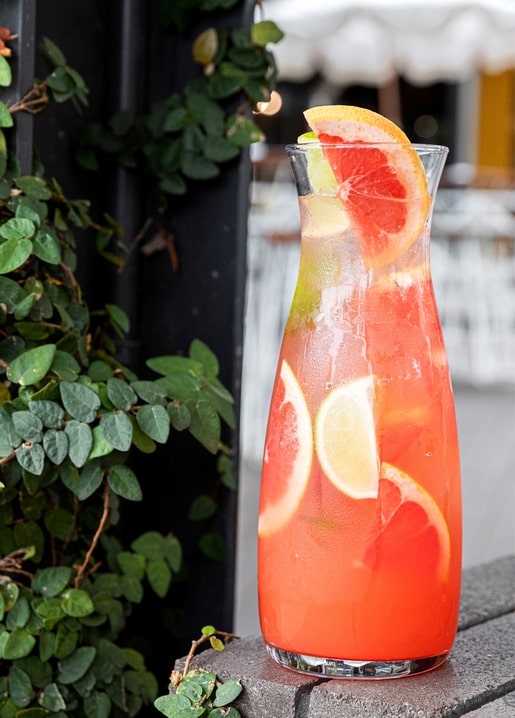 Glaskaraffe mit rosa Grapefruit-Limetten-Limonade und Eis auf einer Café-Terrasse