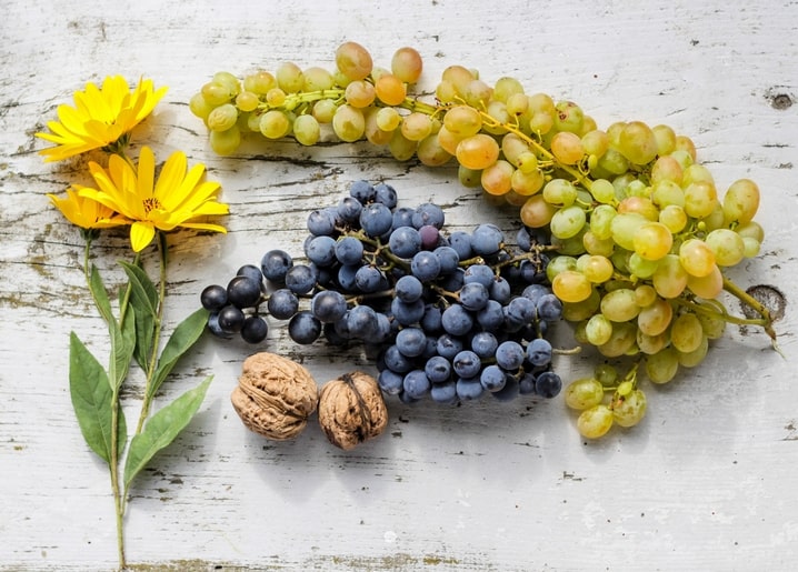 Green and purple grapes, walnuts and yellow flowers on weathered white wood