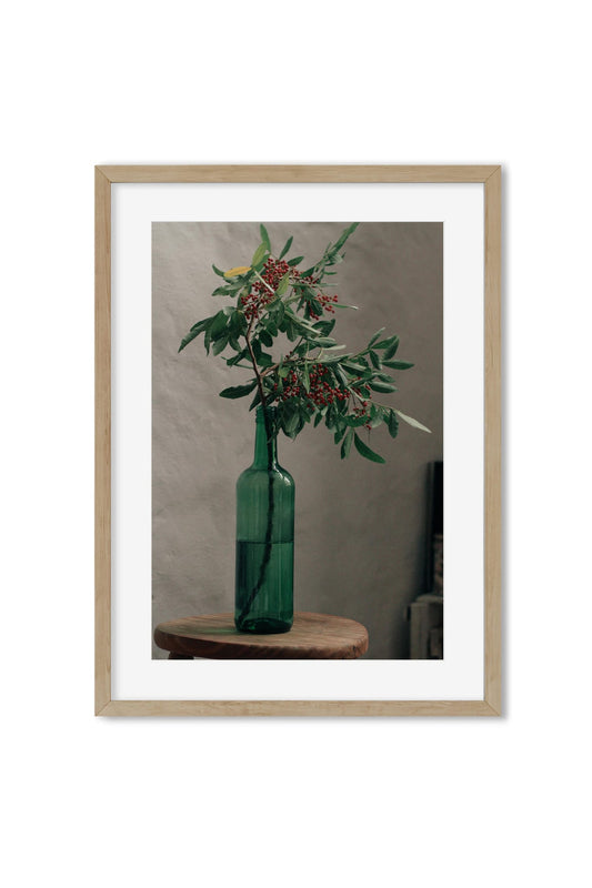 Still life poster of a green glass bottle holding a branch of red berries on a wooden stool