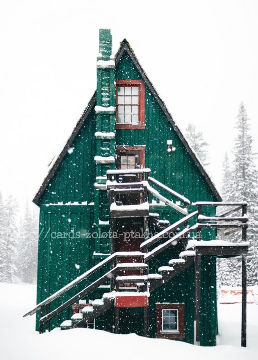 Grüne Holzhütte mit schneebedeckter Wendeltreppe im Schneefall