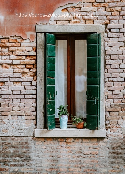 Offenes Fenster mit grünen Fensterläden und zwei Blumentöpfen an einer verwitterten Ziegelwand