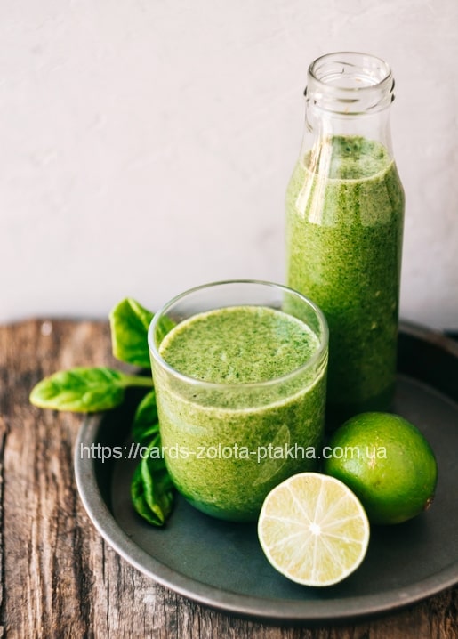 Grüner Smoothie in Glas und Flasche mit Spinat und Limette auf Holztisch