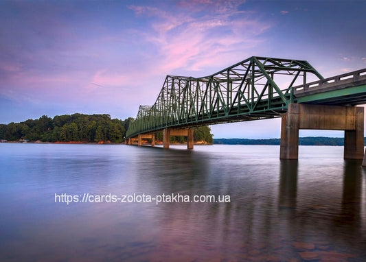 Grüne Stahlfachwerkbrücke über einem See bei rosa Sonnenuntergang