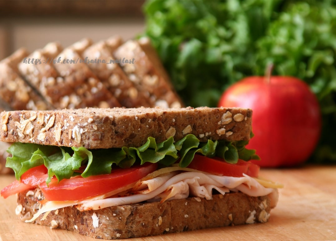 Ham sandwich with lettuce, tomato and cheese beside a red apple