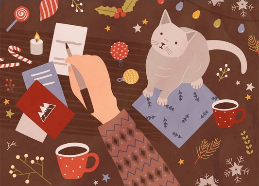 Hand writing a red Christmas card beside a cat and cups of coffee on a dark table