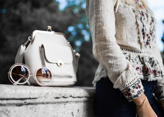 Weiße Handtasche und runde Sonnenbrille mit roségoldenem Rahmen auf einer Steinmauer