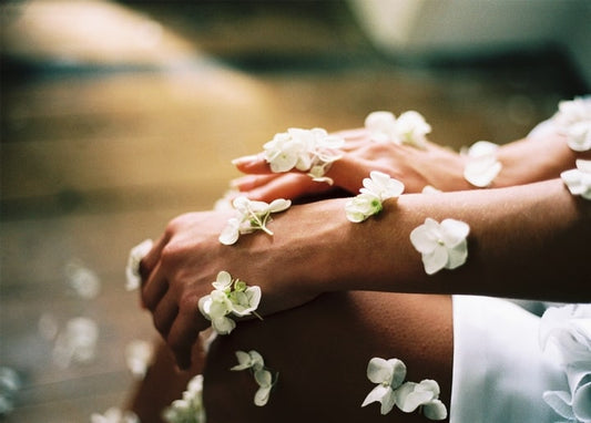 Hands resting in a lap, covered in scattered white flower petals