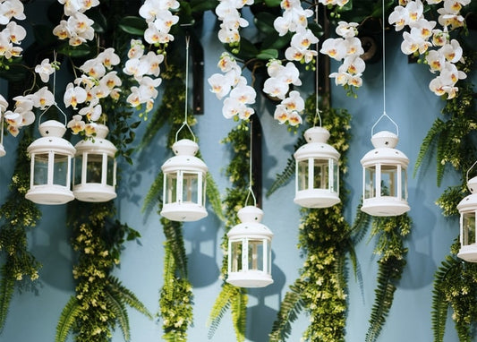 White orchids and ferns hanging above small white lanterns on a blue wall