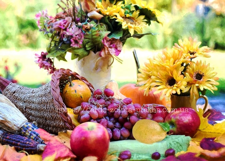 Cornucopia overflowing with pumpkins, grapes and apples beside sunflowers