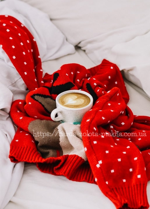 Latte mit Herzmuster in roter Strickdecke auf weißer Bettwäsche
