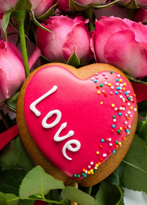 Пряникове сердечко з написом «Love» та цукровою посипкою серед рожевих троянд