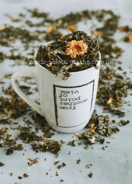 White mug overflowing with dried herbal tea and a daisy, printed with an upside-down quote