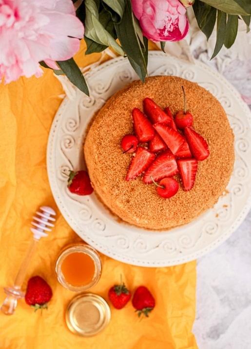 Honigkuchen mit Erdbeeren neben Pfingstrosen und einem Glas Honig