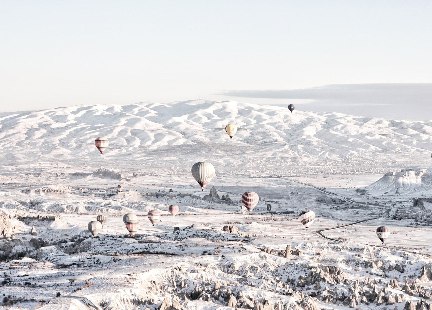 Bunte Heißluftballons schweben bei Sonnenaufgang über einem verschneiten Tal