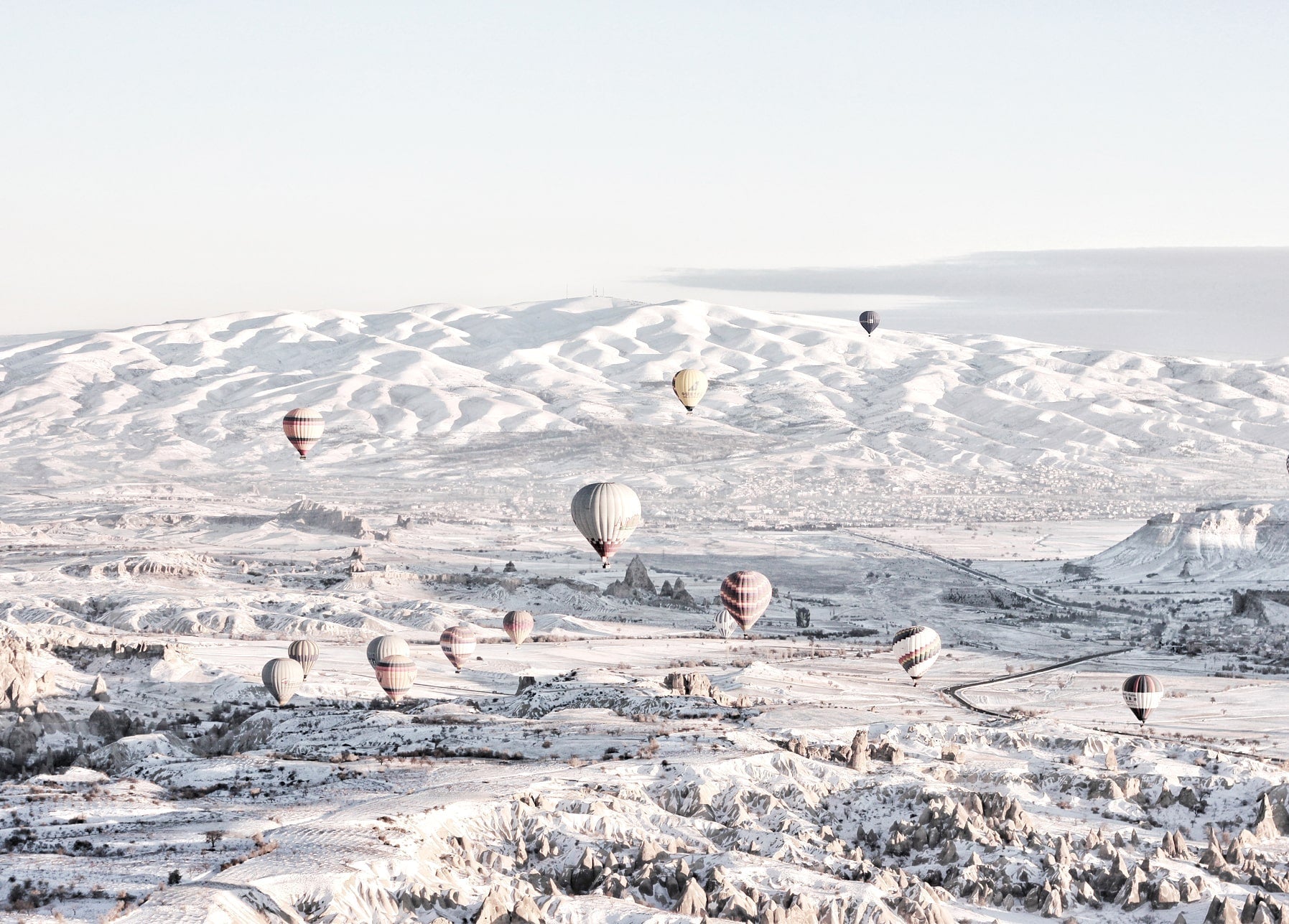 Bunte Heißluftballons schweben bei Sonnenaufgang über einem verschneiten Tal