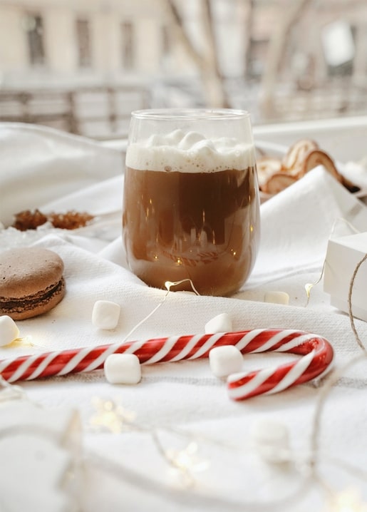 Glass of hot cocoa with marshmallows, candy cane, and macaron on linen