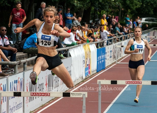 Спортсменка стрибає через бар'єр на легкоатлетичному стадіоні