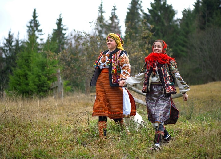 Two women in embroidered Hutsul folk dress crossing a Carpathian mountain meadow