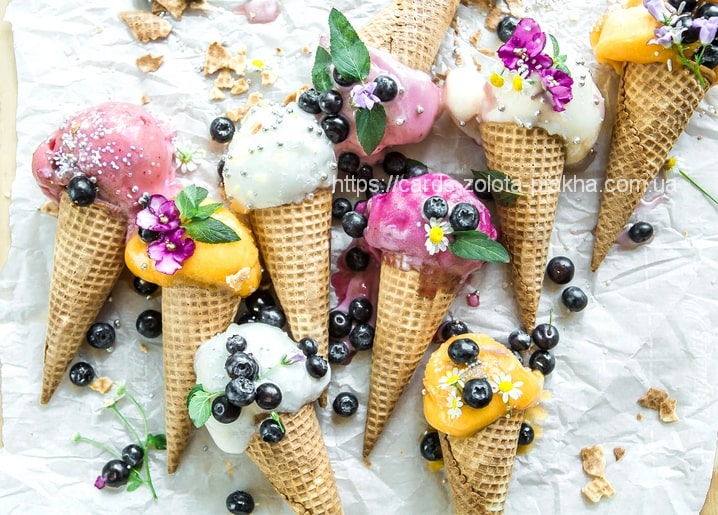 Draufsicht auf verschiedene Eistüten mit Blaubeeren, Minze und essbaren Blüten