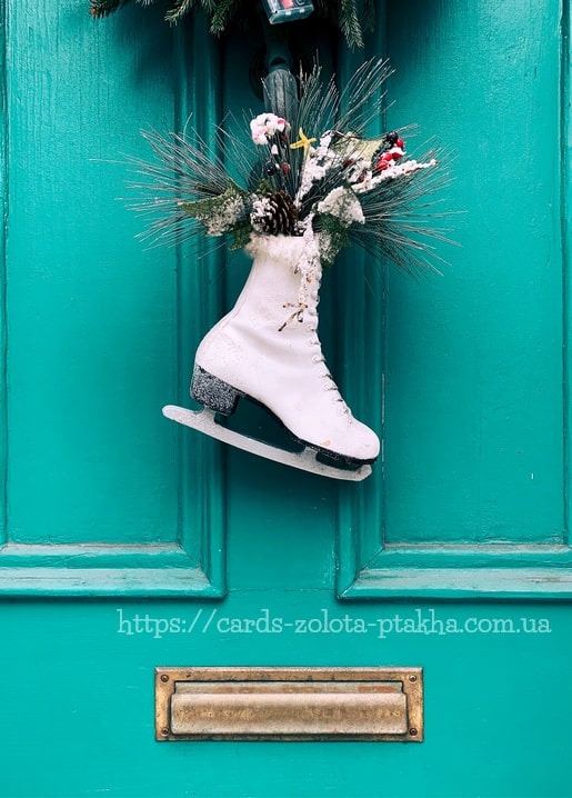 Weißer Schlittschuh mit Tannenzweigen, Zapfen und Blüten an einer türkisen Tür