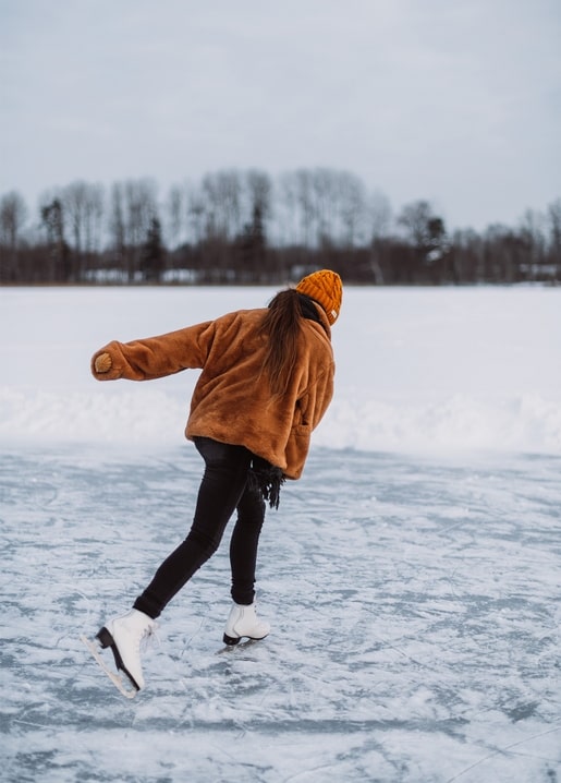 Woman in an orange beanie and teddy jacket ice skating across a frozen lake