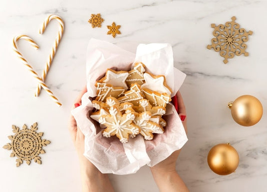 Hände halten eine Schachtel mit Stern- und Schneeflockenkeksen und goldenen Weihnachtsornamenten