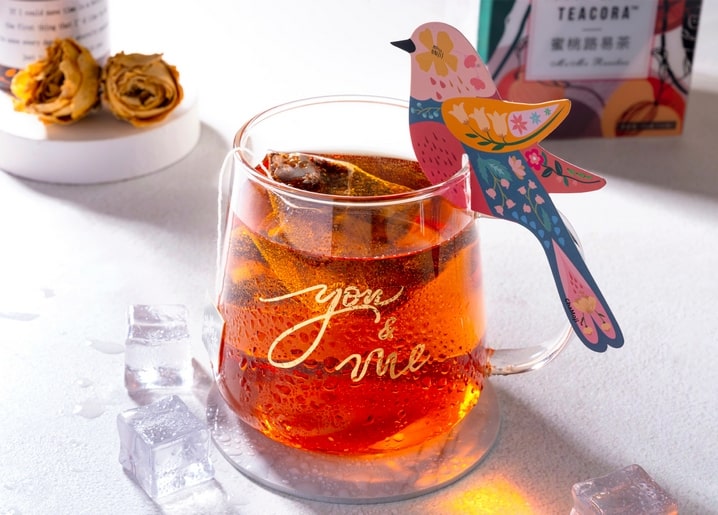 Glass mug of iced tea with a colorful paper bird and gold 'you & me' script