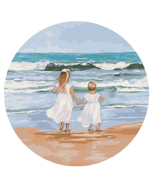 Round painting-by-numbers canvas of two girls in white dresses walking toward ocean waves