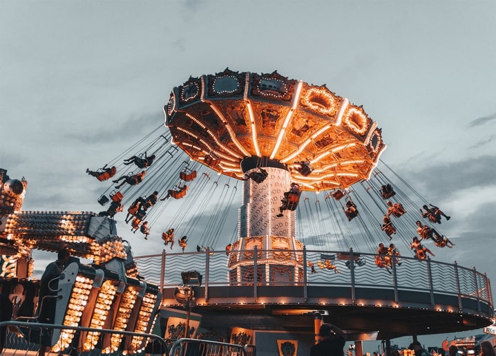 Beleuchtetes Kettenkarussell mit Fahrgästen vor dämmrigem Himmel auf einem Jahrmarkt
