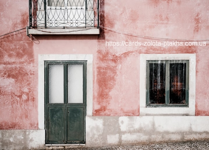 Schmiedeeiserner Balkon über einer Milchglastür an rosa Fassade in Lissabon, Kopfsteinpflaster unten.