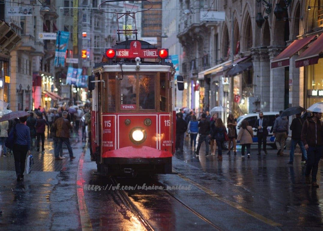 Rote Straßenbahn auf der Istiklal-Straße in Istanbul im Regen bei Dämmerung, Passanten mit Regenschirmen