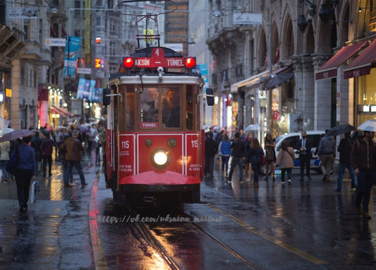 Rote Straßenbahn auf der Istiklal-Straße in Istanbul im Regen bei Dämmerung, Passanten mit Regenschirmen