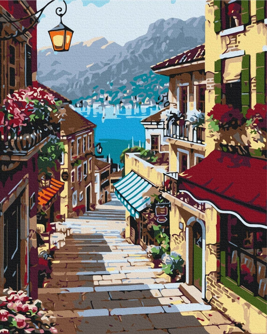 Italian coastal street lined with flowers and café awnings above a turquoise bay