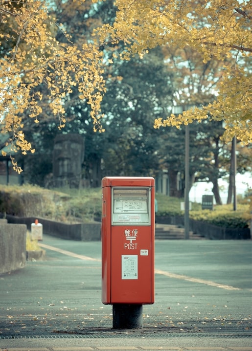 Red Japanese post box on a path beneath golden ginkgo trees in autumn
