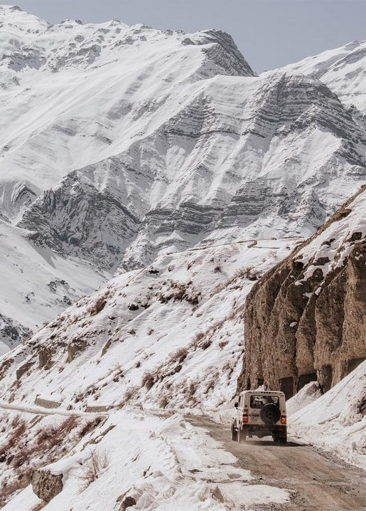 Weißer Geländewagen fährt eine schmale Straße durch einen verschneiten Bergpass