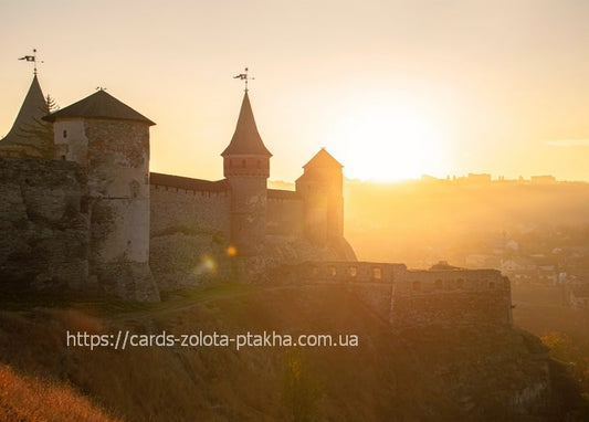 Silhouette of Kamianets-Podilskyi Castle towers against a golden sunset sky
