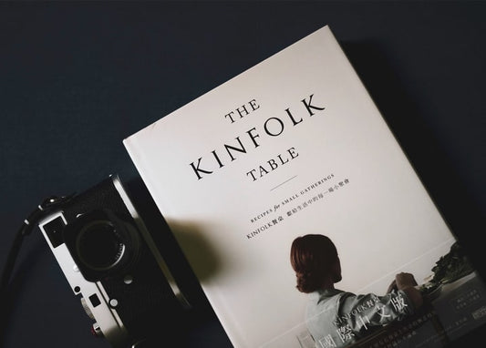 Stillleben mit dem Buch „The Kinfolk Table“ und einer Vintage-Kamera auf Schwarz.