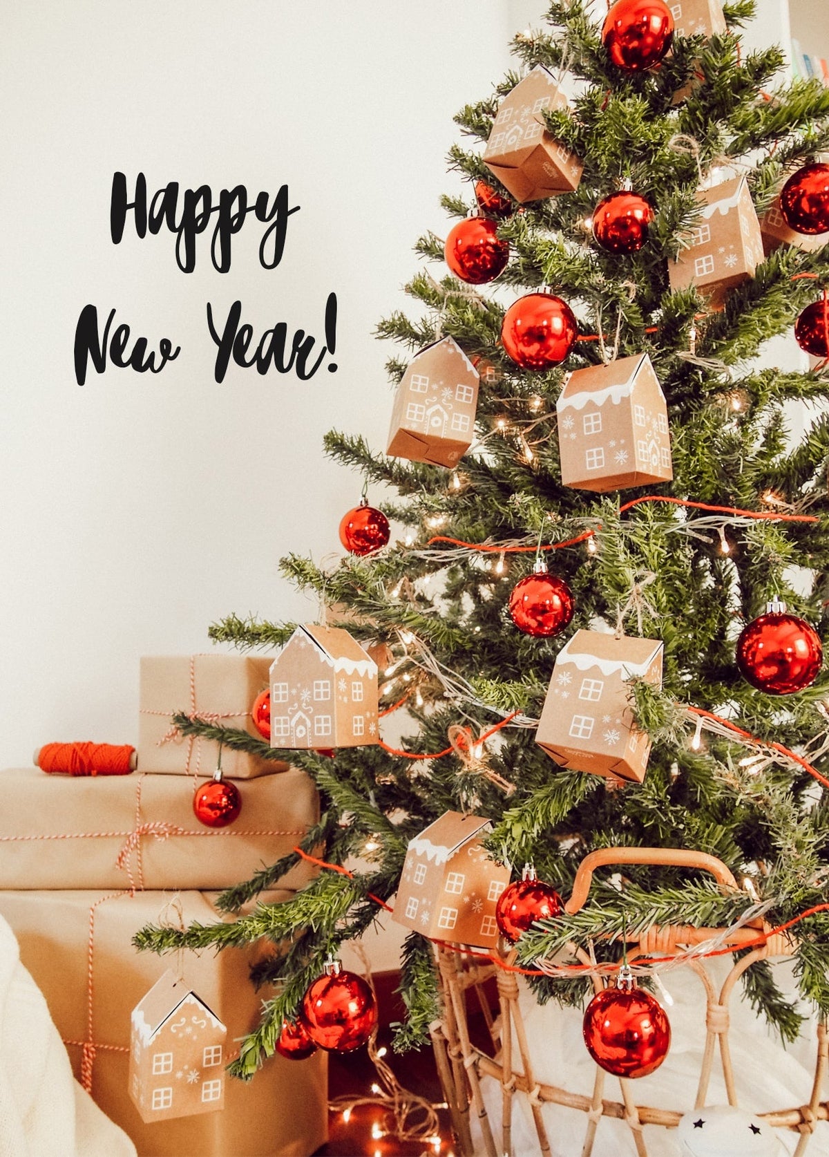 Kraft-paper house ornaments and red baubles on a lit Christmas tree with gifts below
