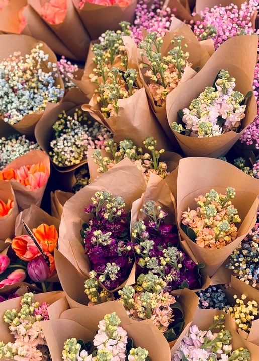 Overhead view of dozens of bouquets wrapped in kraft paper, featuring orange tulips and purple stock flowers.