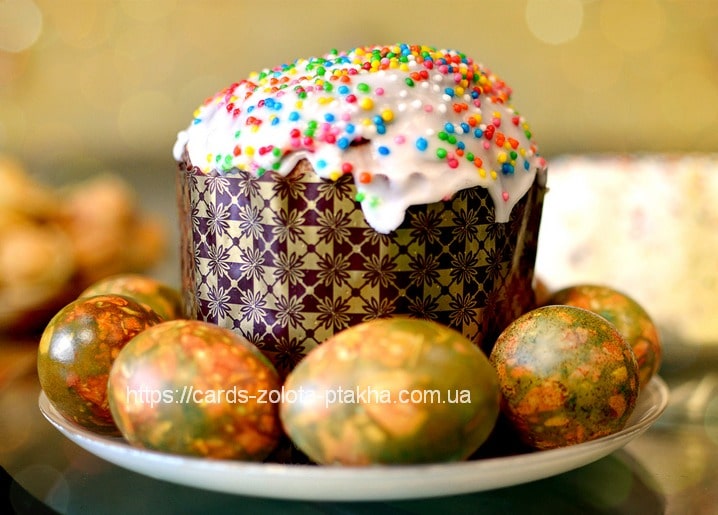 Kulich in a patterned wrapper surrounded by marbled green and orange dyed eggs on a plate