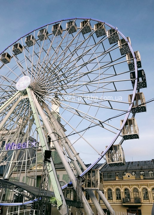 Large Ferris wheel against a blue sky with a historic building in the background, Kyiv
