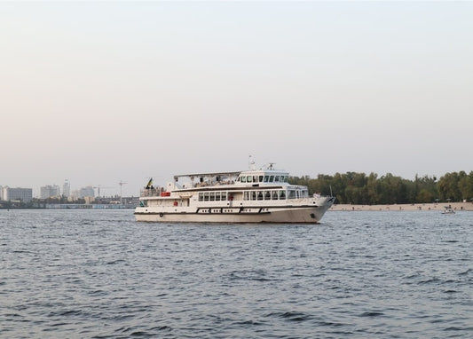 Weißes Ausflugsboot auf dem Dnipro in der Dämmerung vor der Skyline Kyjiws
