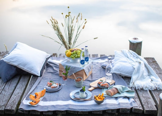 Picknickdecke mit Trauben, Melone und Getränken auf einem Seesteg