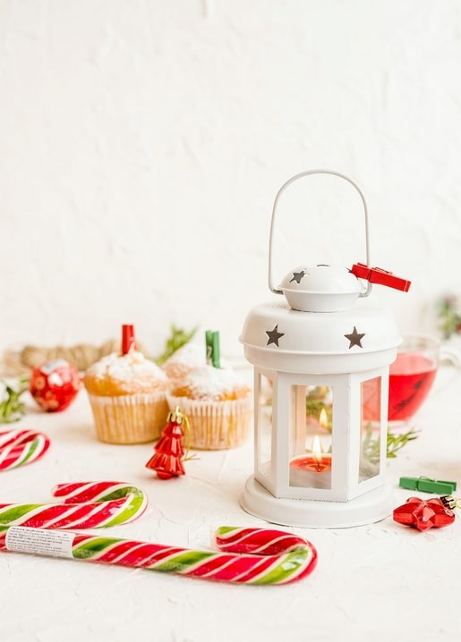 Weiße Laterne mit Kerze neben Zuckerstangen und gezuckerten Cupcakes