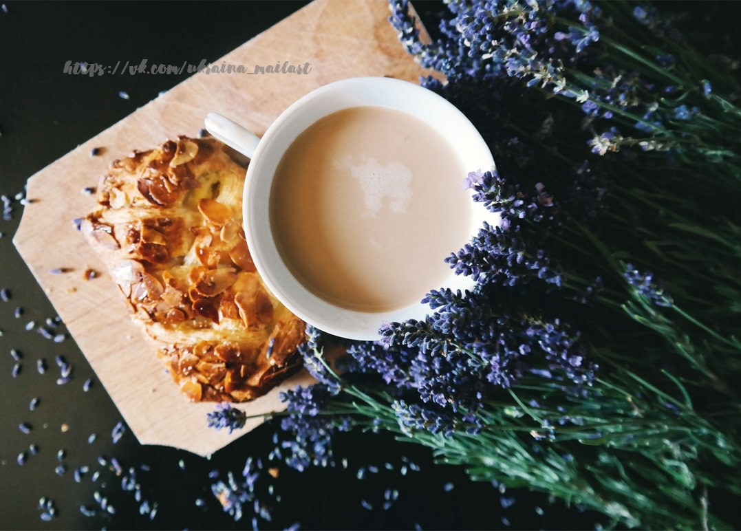 Milchkaffee und Mandelgebäck auf Holzbrett neben einem Lavendelstrauß